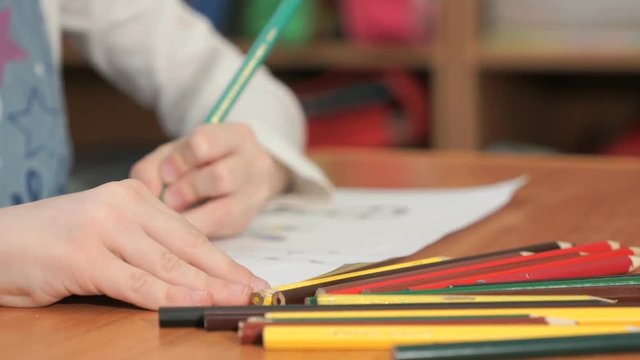 Close-up of unknown little girl draws the pictures using color pencils in the album in the kindergarten