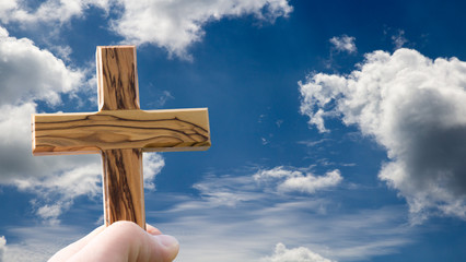 Hand hält Holzkreuz in den Himmel