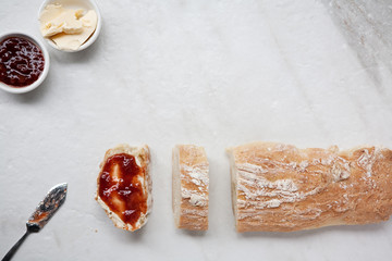 Flat lay of homemade french bread baguette sliced with strawberry jam and butter 