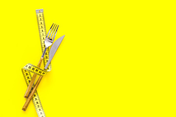 Diet, weight loss, slimming concept. Fork and knife with wound measuring tape on yellow background top view space for text