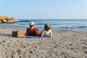 Joven pareja haciendo un picnic junto al mar al atardecer