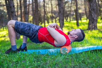 Fototapeta na wymiar Handsome healthy man doing an exercise on a mat with foam roller on his upper back.