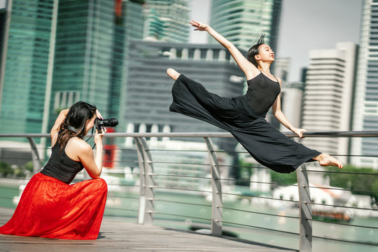 Two beautiful young girls having fun photo shooting on a deck with skyscrapers city background