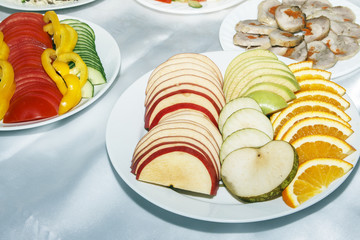 Sliced red and green apple and orange on white plate. Fresh snack for reception guests on festive table. Copy space