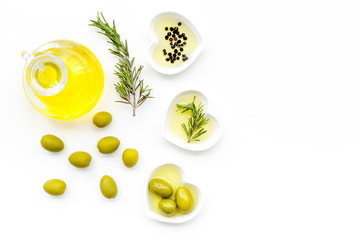 Fresh olive oil in glass jar near green olives and branch of rosemary on white background top view...
