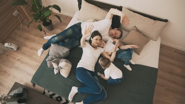 Cute family playing on bed at home in bedroom in slow motion. Top view. Happy family concept. Young family have fun indoor