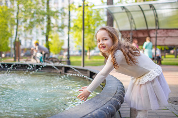 Cute little girl playing by city fountain on hot and sunny summer day. Child having fun with water in summer. Active leisure for kids.
