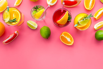 Tropical fruit cocktail with alcohol. Glass with beverage near oranges, grapefruit, lime and rosemary on pink background top view copy space