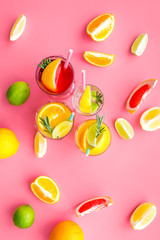Tropical fruit cocktail with alcohol. Glass with beverage near oranges, grapefruit, lime and rosemary on pink background top view pattern