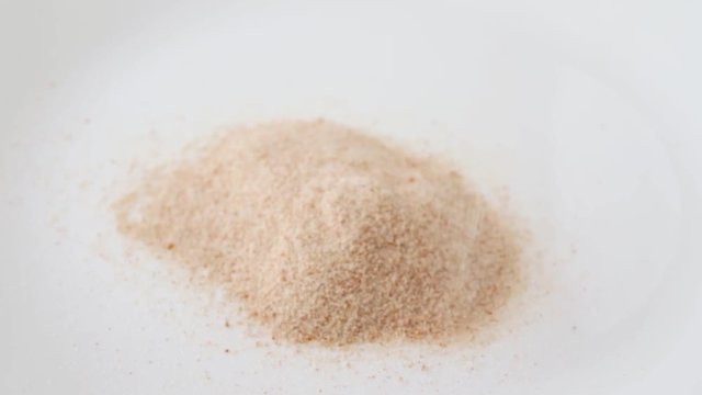 Close video of pouring orange flavored psyllium husks onto a white plate.