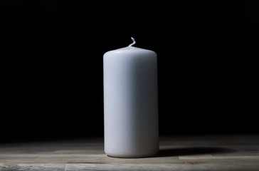 White wax candle on wooden surface with black background - lit from the side