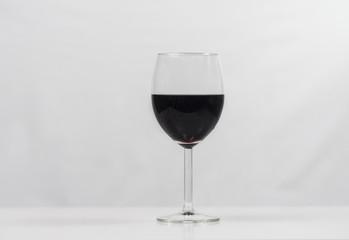 A glas of dark red wine on shiny white table with a white cloth as background