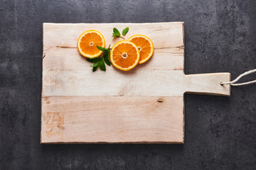 Flat lay of fresh citrus fruits, half cut orange slices on cutting board on black stone background. Horizontal top view with copy space.