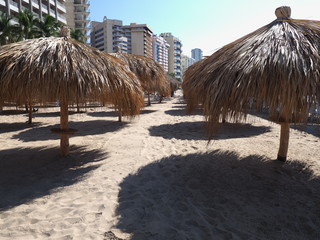 Scenic bamboo umbrellas on sandy beach at bay of ACAPULCO city in Mexico with hotel buildings