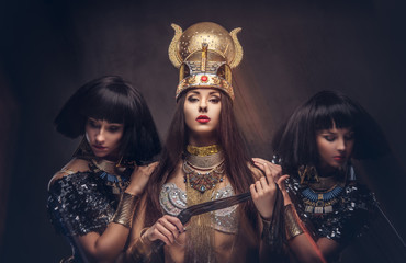Portrait of haughty Egyptian queen in an ancient pharaoh costume with two concubines.
