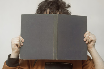 little boy hides his face behind a book