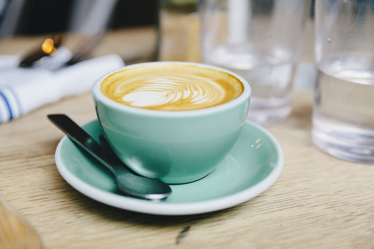 Close-up Of Frothy Drink Served In Coffee Cup On Wooden Table At Cafe