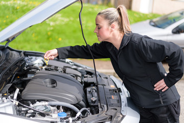 A woman mechanic checking a car's oil level at roadside