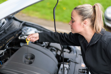 Fototapeta na wymiar A woman mechanic checking a car's oil level at roadside