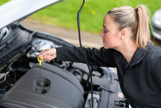 A woman mechanic checking a car's oil level at roadside - Powered by Adobe
