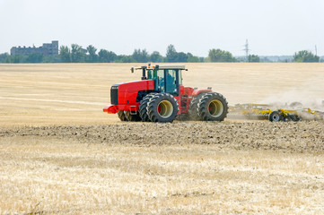 Tractor preparing land with plow, sunny summer day at agricultural field