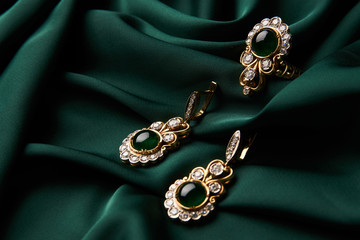 Beautiful Golden ring and pair of earrings with green Emerald and Diamonds gemstones on a green...