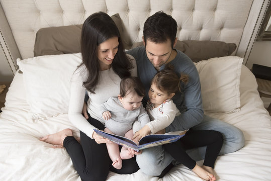 High angle view of parents with children looking at picture book while sitting on bed