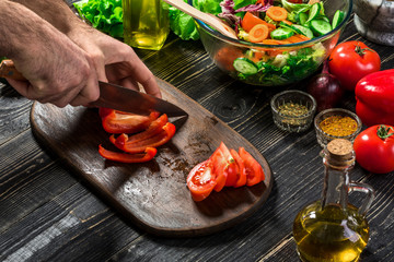 Man's hands cutting red paprika with knife. Cook cut red paprika. Man loves cooking fresh salad for dinner. Paprika cut by cook's hand.