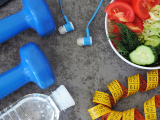 Dumbbells, measuring tape, water, telephone with headphones, bowl with salad. The concept of fitness, healthy eating and active lifestyle.
