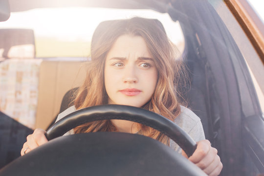 Nervous Female Driver Sits At Wheel, Has Worried Expression As Afraids To Drive Car By Herself For First Time. Frightened Woman Has Car Accident On Road. People, Driving, Problems With Transport