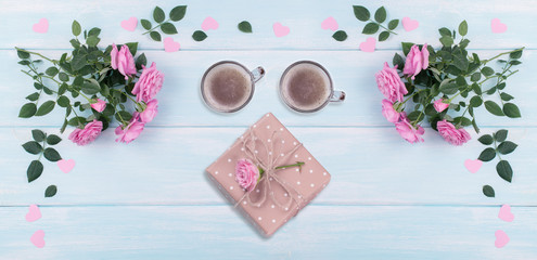 Top view of pink roses, two coffee cups and gift box with paper hearts