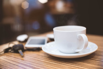 Cup of hot coffee , Key and smartphone in cafe.Selective focus
