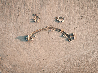 A sad smiley drawn on the sand. Depression concept.