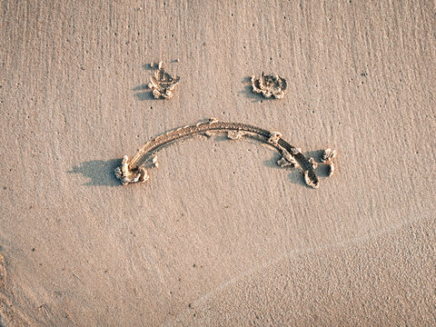A sad smiley drawn on the sand. Depression concept.