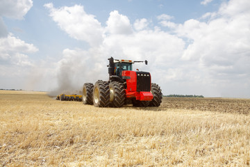 Tractor preparing land with plow, sunny summer day at agricultural field