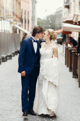 Naklejka premium Newlywed couple kiss outdoors in town street, family portrait - beautiful bride kissing with handsome groom while on a walk in France