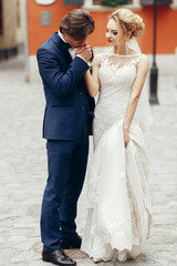 Romantic groom kissing hand of beautiful happy bride outdoors, newlywed couple portrait