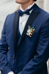 Handsome groom portrait, smiling groom in elegant blue suit with boutonniere posing outdoors close-up, man wedding fashion concept