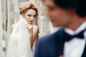 Naklejka premium Gorgeous, sexy bride looking at happy handsome groom, newlywed couple portrait, beautiful bride face looking at stylish groom in suit, emotional wedding moment