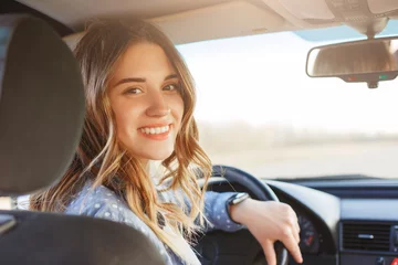 Foto op Canvas Close up portrait of pleasant looking female with glad positive expression, being satisfied with unforgettable journey by car, sits on driver`s seat, enjoys music. People, driving, transport concept © sementsova321