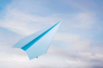 Blue paper plane agains cloudy sky