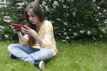 Beautiful teenager girl with tablet computer sits on the grass in Park. Photo
