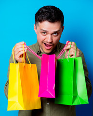 Young man holding a colorful shopping bags on blue background