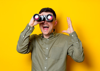 Young man looking for something with binoculars on yellow background