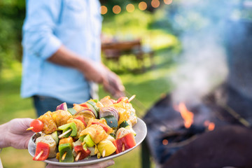 In summer. A couple prepares a bbq to welcome friends in the garden. Close-up on a plate of grill skewers