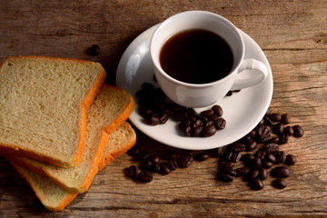 Coffee cup with sliced bread and fresh coffee beans on wooden table.