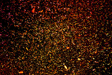 Confetti fired in the air during a beach party. Only confetti on black background of the night. Confetti red and yellow