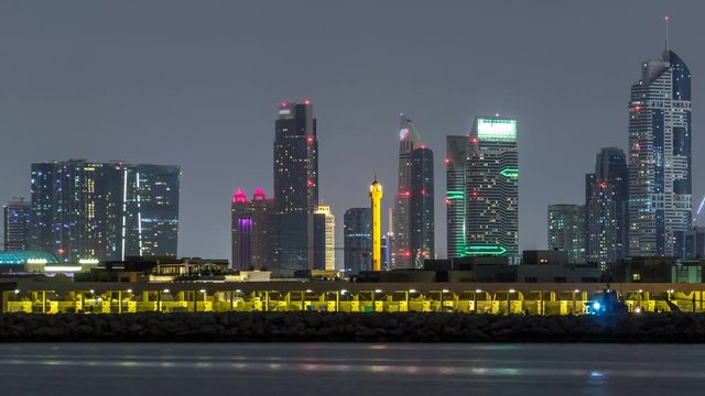 Modern Dubai city skyline timelapse at night with illuminated skyscrapers over water surface
