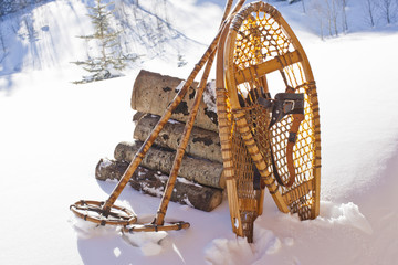 Wooden snow shoes and snow poles leaning against a stack of cut firewood in the snow.
