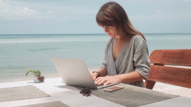 Young Woman works on laptop in outdoor cafe, moving camera, stabilizer shot